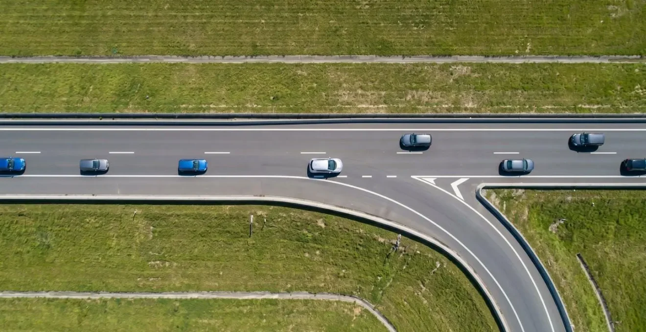 Vue aérienne minimaliste d'une bretelle d'insertion sur périphérique montrant la trajectoire fluide d'un véhicule électrique